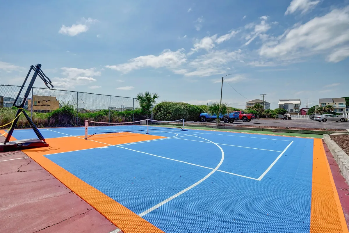 This exterior shot features a vibrant basketball court with a visible hoop and a tennis net, set against a backdrop of greenery. The area is spacious and ideal for both sports and group games, inviting guests to engage in both basketball and tennis matches under the sun.