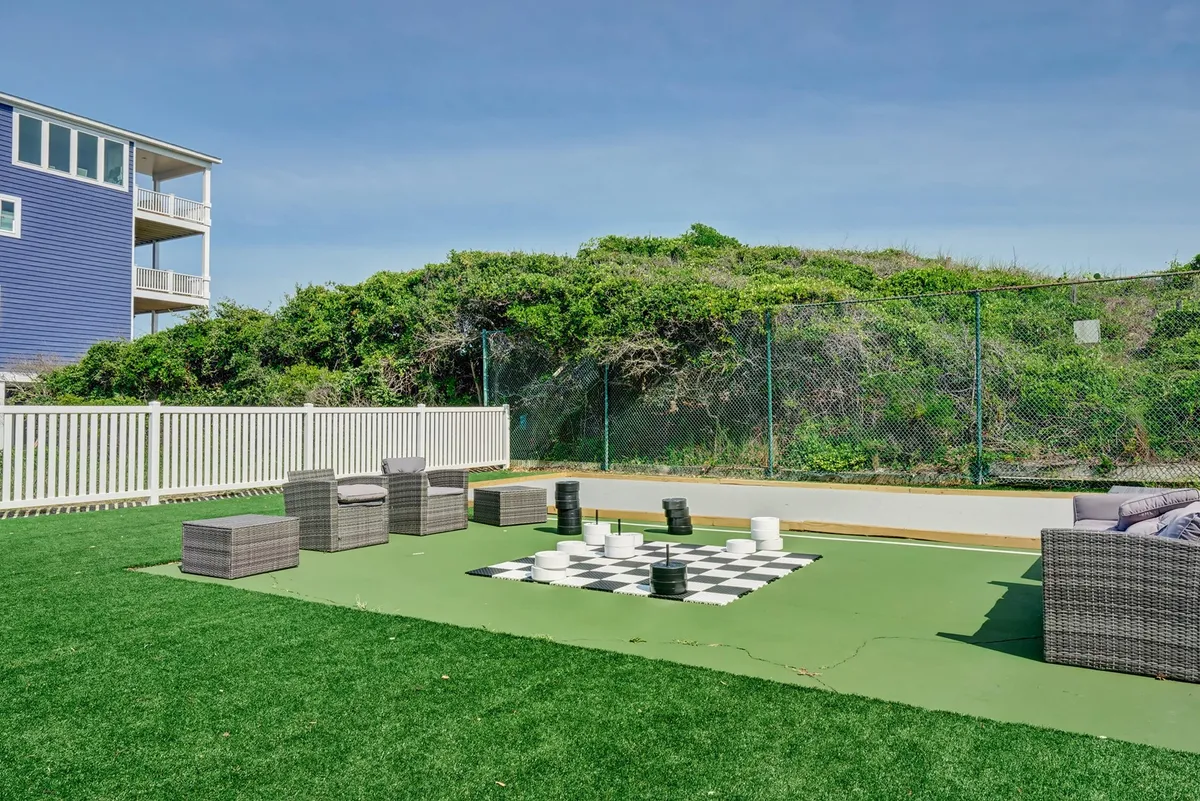 This exterior image features a large outdoor chessboard surrounded by comfortable seating and lush greenery, inviting guests to enjoy playful activities and social gatherings in the sun. The area feels relaxed and open, perfect for casual group fun after a day of exploring Topsail Island.