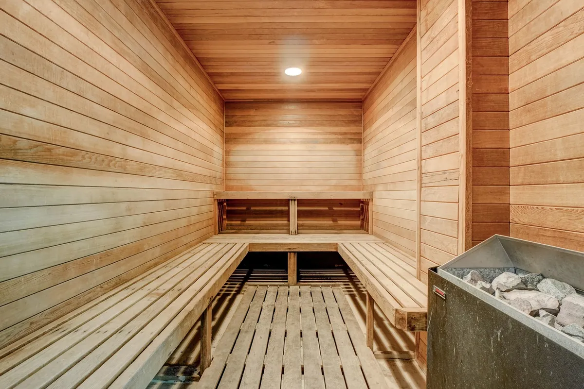 A tranquil sauna space featuring wooden benches, a stone heater, and calming wooden paneling. The design encourages relaxation and meditative wellness routines, creating a peaceful retreat within the property.